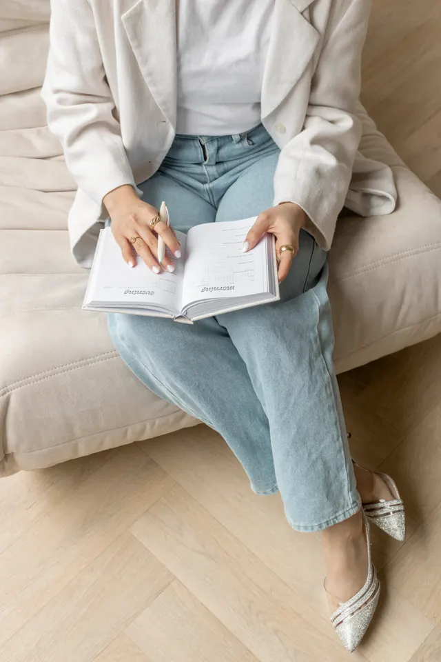 Mulher com caderno no colo e calça jeans