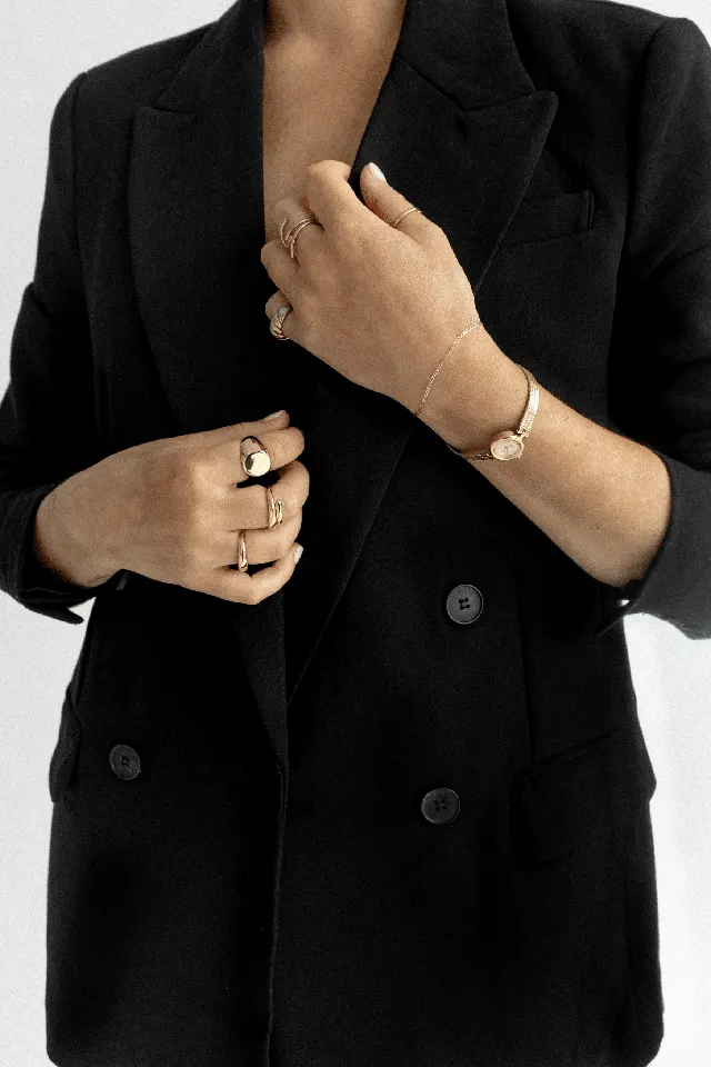 Detalhe de blazer preto, anéis e colar